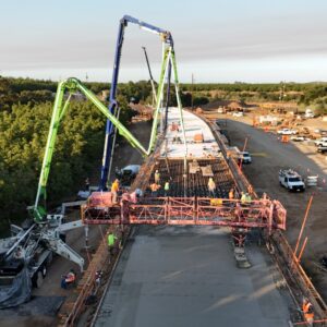 A high vertical view of a green and blue boom pump extending delivery lines and pouring concrete over grid of steel reinforcing rebar.