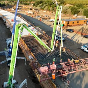 Green and blue boom pumps extending delivery lines and pouring concrete over grid of steel reinforcing rebar.