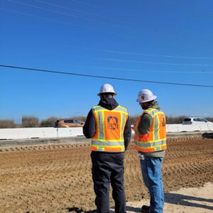 Two men in PPE standing next to the leveled dirt road.