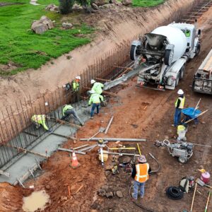 A crew of workers in PPE smoothing concrete from a concrete truck.