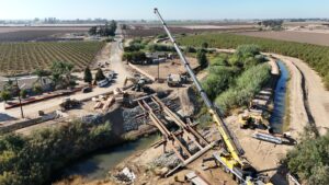 A crane on the right side of the bridge placing falsework beams and equipment on both sides.