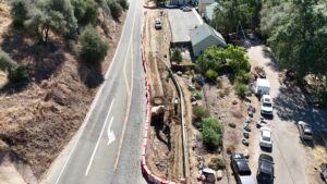 An excavator starting to level out a dirt road between a retaining wall and red k-rail.