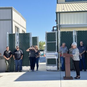 A women speaking at a podium with other people beside her watching.