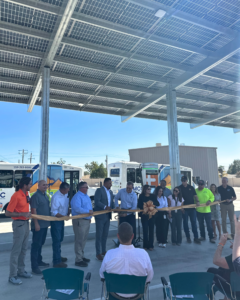 Group of people standing in a row behind a golden ribbon for a ribbon cutting ceremony.