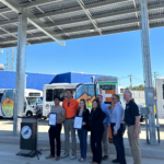 Group of people smiling and holding certificates to celebrate the ribbon cutting.